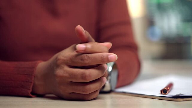 A close-up of a stressed woman sitting at a desk with clasped hands, suggesting emotional pressure, workplace anxiety, and personal insecurity. Suitable for themes of mental health, stress management,