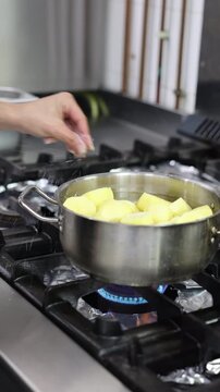 Hands peeling a raw potato with a knife over a pot of peeled potatoes