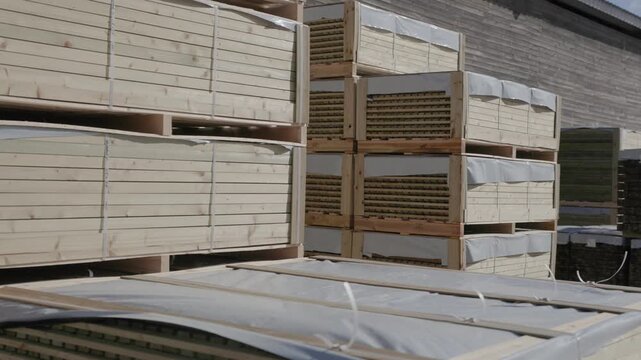 Bundled wooden boards stacked outside a warehouse under clear sky. Copyright: no people or visible logos; property release may be needed