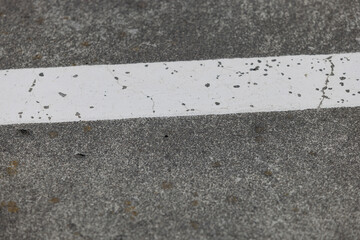 Fototapeta premium A white marking stripe on cracked grey concrete, a close abstract view of a parking deck floor.