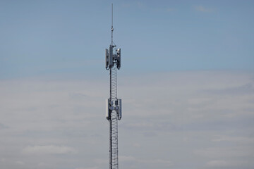 Obraz premium A tall lattice communications mast with cellular antennas rises against a pale blue sky.