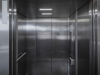 The brushed stainless steel interior of a modern elevator with reflective walls and ceiling lights. © Victor