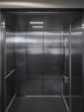 The empty brushed metal interior of a lift with polished walls reflecting the ceiling lights.