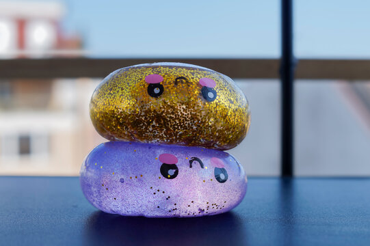 Gold and purple glitter squishy toys with smiling faces rest together on a tabletop. Sensory toy concept for stress relief, tactile play and cheerful childhood mood