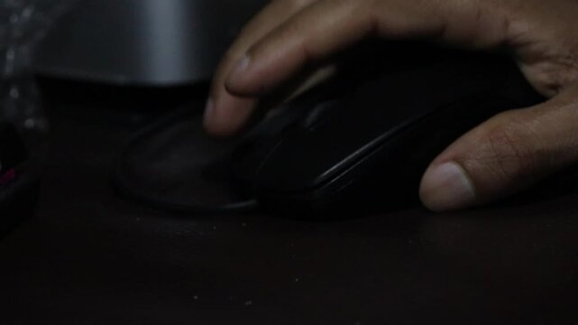 Close up of a hand holding and clicking a black computer mouse in a dark room