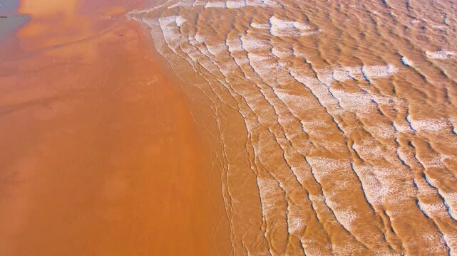 Elevated bird's-eye view of beautiful brown sand coastline and textured water foam patterns
