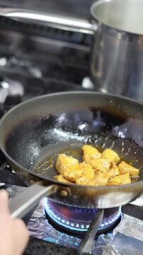 Chicken pieces cooking in a frying pan over a blue gas flame on the stove