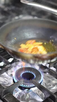 Chicken pieces cooking in a frying pan over a blue gas flame on the stove