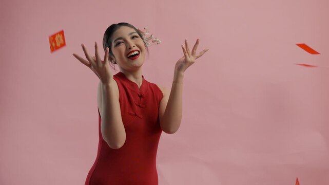 Excited young Asian woman is throwing angpao or red packet monetary gift, isolated by pink background.