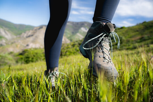 Close-up of a woman's legs and hiking boots, stepping through green grass in the mountains on a sunny summer day.