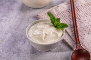Creamy yogurt in white bowl with fresh mint leaf on textured surface © Andrei Starostin
