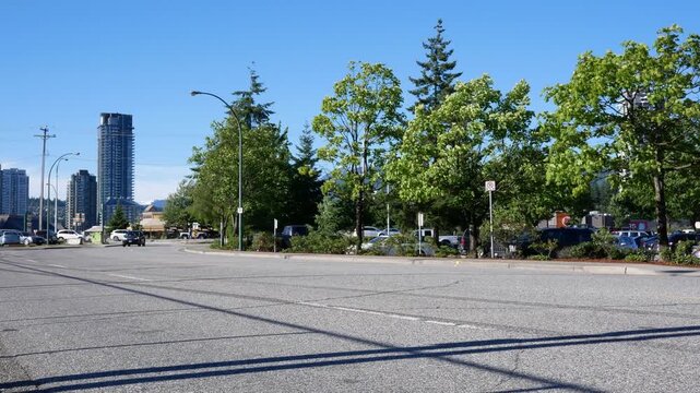 Red SUV and Dark SUV Driving on Urban Road with Cityscape and Green Trees on a Sunny Day