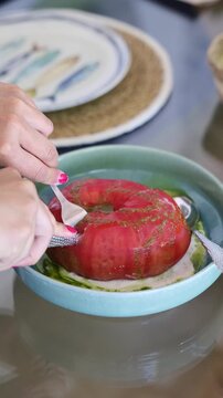 Person using fork and knife, preparing to eat fresh gourmet tomato salad with sauce in bowl