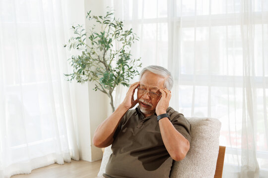 Elderly Man Suffering from Headache While Sitting at Home. Elderly Man Feeling Dizzy and Touching His Temples While Seated Indoors.