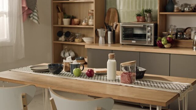 Close up of breakfast table featuring fresh apples, milk bottle, and cereal jars standing in modern kitchen. Video ideal for healthy lifestyle ads or kitchenware brand promotions