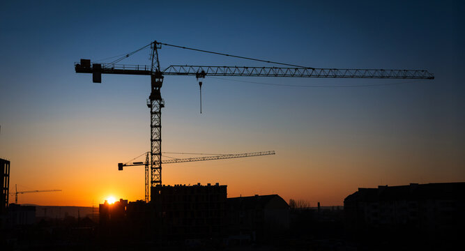 Construction cranes silhouetted against a vibrant sunset sky on a clear evening