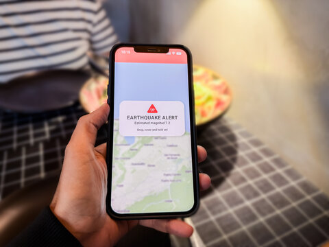 Person using earthquake app on mobile phone for real-time emergency alert - High magnitude warning