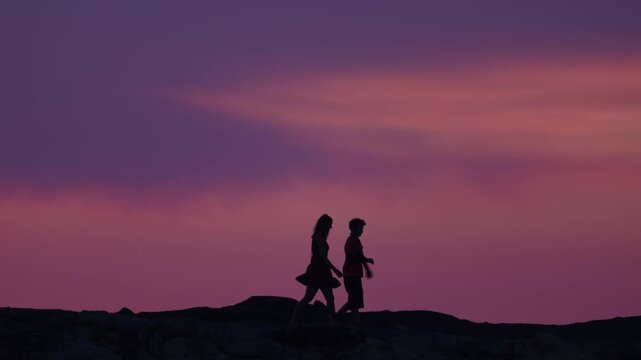 Silhouette of a mother and her 11 year son with an arm brace walking on a stone pier during the pastel blue hour. Inspiring family video of a medical recovery journey and an evening stroll by the sea