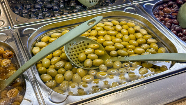 Marinated green olives in a stainless deli tray under warm market light for editorial food blog restaurant menu grocery Mediterranean mood, 5 May 2026 Subitica, Serbia