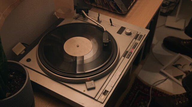 Vintage turntable spinning black vinyl record on wooden table next to houseplant. Footage for retro music equipment ads, nostalgic lifestyle promos, or audio store marketing campaigns