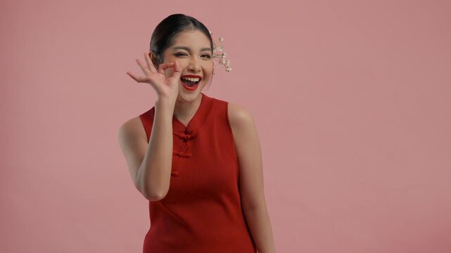Excited young Asian woman wearing traditional cheongsam qipao dress showing okay finger gesture, isolated by pink background.