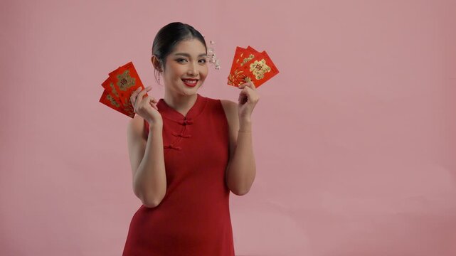 Cheerful young Asian woman is smiling and holding angpao or red packet monetary gift, isolated by pink background.