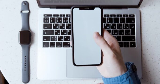 Hand holding smartphone with blank white screen over laptop keyboard