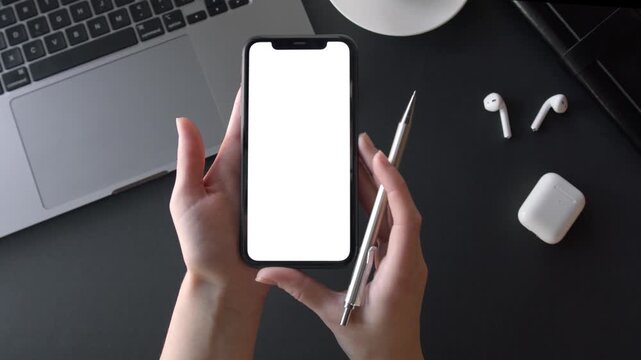 Hands holding smartphone mockup with blank screen on dark desk