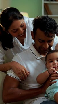 Parents sitting with baby boy while sitting on floor near sofa in modern living room, showcasing Indian family bonding, love, parenting, parenthood, emotional care, happy lifestyle, and cozy moments