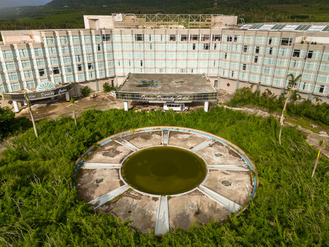 Aerial view of the derelict Tinian Dynasty Hotel featuring an abandoned circular fountain surrounded by overgrown tropical vegetation in San Jose, Tinian, Northern Mariana Islands.