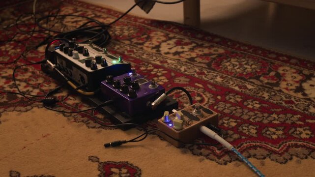 Guitar effects pedals resting on patterned rug with glowing LED lights indicating active power. Clip for music production tutorials, gear reviews, and home studio marketing campaigns
