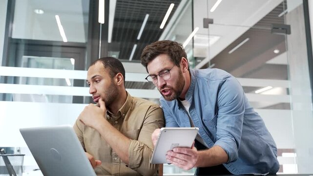 Angry boss quarreling with male subordinatesitting at workplace in business office. Furious executive arguing at young employee talking about problems. Dissatisfied manager unhappy with work results