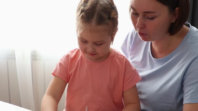 Young woman and child collaborating on colorful handmade postcards in a warm indoor setting. Learning, creativity, and bonding concept. Mid shot