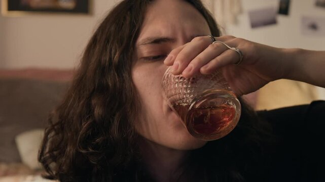 Close-up rack focus shot of young man swirling whiskey in glass, drinking and grimacing. Perfect for commercial videos addressing alcoholism, depression, mental health struggles