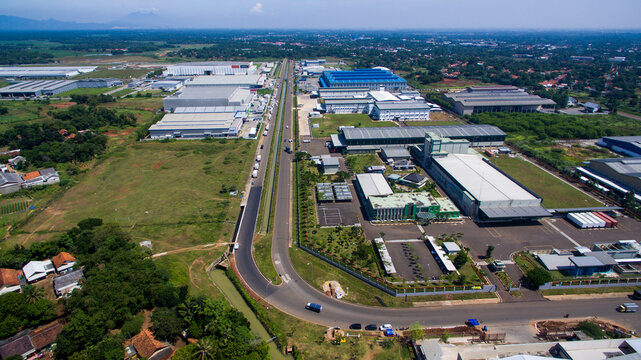 Aerial view of the Mekarwangi Industrial Estate featuring large factory buildings, warehouses, and road infrastructure surrounded by green landscapes in Cikarang Barat, West Java, Indonesia.