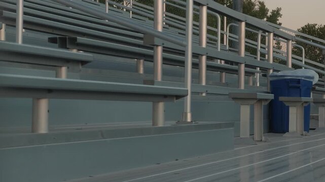 Slow left to right glide past empty stadium bleachers with a foreground pole creating layered depth.