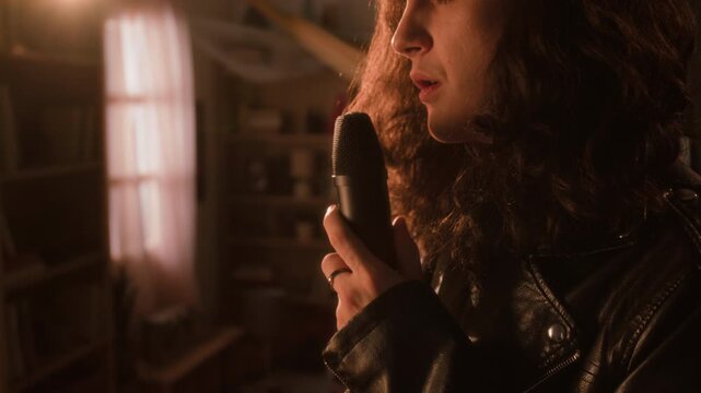 Young man with long curly hair wearing leather jacket singing passionately into microphone. Clip for music industry promos, audio gear ads, or creative lifestyle campaigns