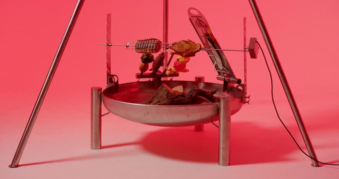 A hand uses stainless steel tongs to arrange raw sausages on a circular barbecue grill grate