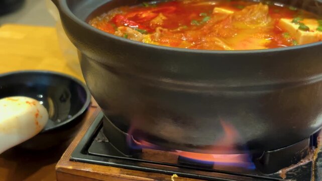 A close-up, static shot of a delicious and spicy Asian hot pot or stew simmering intensely inside a black cooking pot.