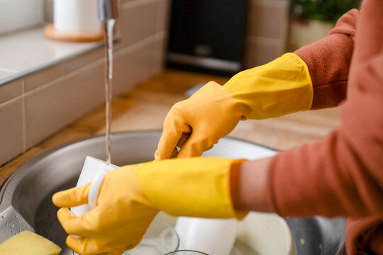 Person washes dishes in a kitchen sink while wearing yellow rubber gloves during daytime