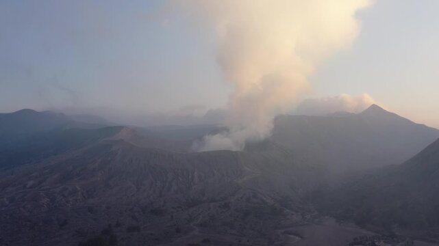 Aerial drone moves in close on smoke rising from the crater of active Mount Bromo at sunrise, East Java, Indonesia. Cinematic close-up of a smoking volcano in golden morning light.