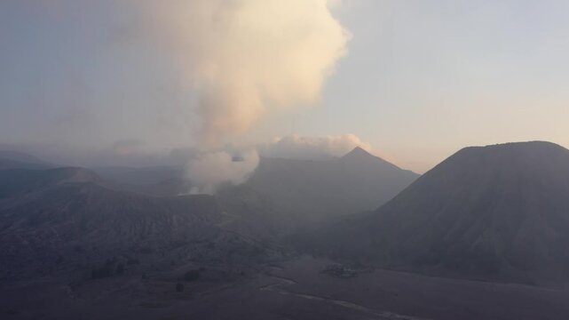 Aerial drone moves slowly toward the active Mount Bromo volcano as smoke rises from its crater in East Java, Indonesia. Cinematic close approach to a smoking volcanic landscape.