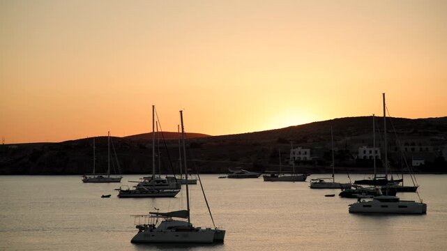 Colorful sunset over calm coastal waters with sailboats drifting peacefully beneath a glowing evening sky