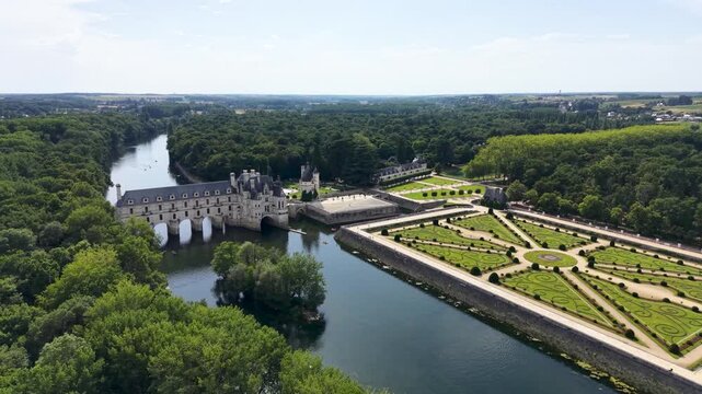 Cinematic drone aerial panorama of Ch&acirc;teau de Chenonceau spanning the River Cher, showcasing the formal French gardens, Renaissance architecture, surrounding forests