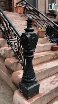 Ornate iron newel post and brownstone stoop with potted flowers in urban setting