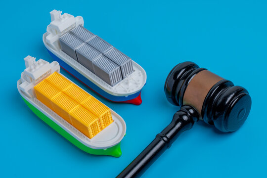 Miniature cargo ships next to a wooden gavel. Maritime law, international trade regulations, shipping disputes, customs tariffs, export embargoes concept.