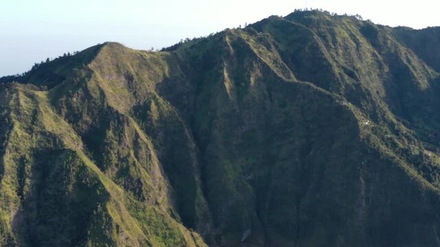 Drone pans left over green mountain ranges surrounding the Mount Bromo area, with small patches of farmland on the slopes below, East Java, Indonesia. Cinematic highland landscape b-roll.