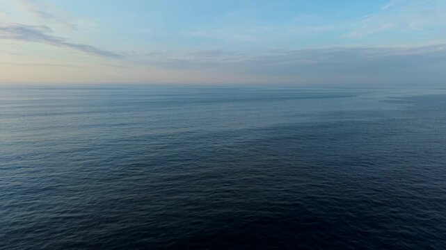 Calm ocean water under a blue sky at sunrise or sunset, tranquil seascape view