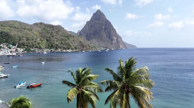 Majestic drone aerial view of the volcanic Pitons peaks behind palm trees on a sunny day in Saint Lucia, Caribbean