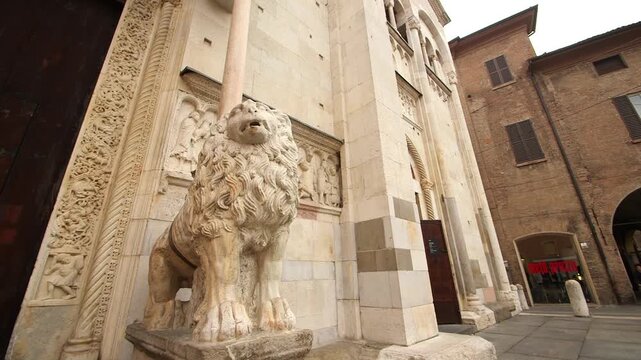 Cinematic slider shot of the stone lion guarding the entrance of Modena Cathedral. Romanesque architectural detail in the UNESCO historic center of Modena, Italy.